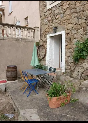 a table and chairs and an umbrella in front of a building at Maison typique village corse in Sari-dʼOrcino