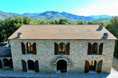 an old brick building with windows and mountains in the background at Un étage entier - 5 chambres indépendantes et 3 salles de bains in Corte