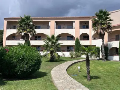 a large building with palm trees in front of it at Soleil corse et tranquillité près de la plage à Marine de Bravone in Linguizzetta
