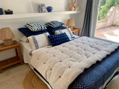 a bed with blue and white pillows and a window at Villa bord de plage à pied proche Pinarello in Sainte-Lucie de Porto-Vecchio
