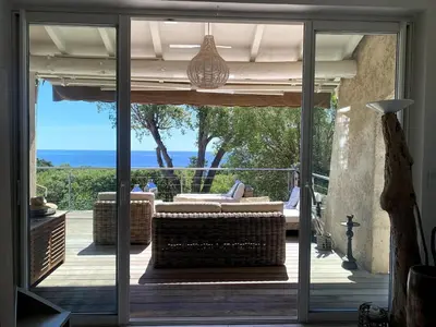 a sliding glass door to a patio with a view of the ocean at Villa bord de plage à pied proche Pinarello in Sainte-Lucie de Porto-Vecchio