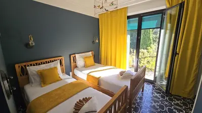 two beds in a room with yellow curtains and a window at Appart'hotel Fior Di Ribba in Sartène