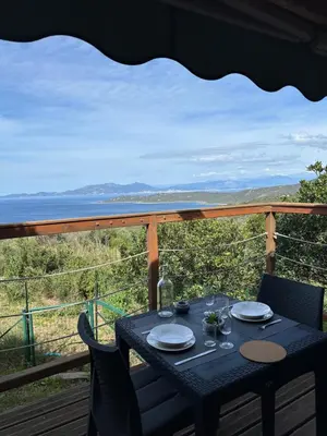 a table on a deck with a view of the ocean at Chalet La Doulou Calme, Vue mer et jardin in Coti-Chiavari