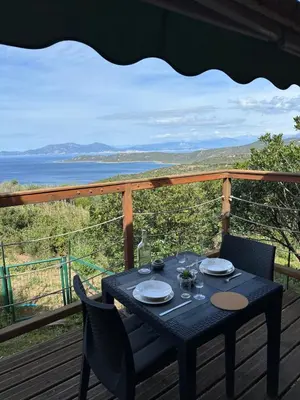 a table on a deck with a view of the ocean at Chalet La Doulou Calme, Vue mer et jardin in Coti-Chiavari