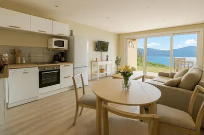 a kitchen and a living room with a table and a couch at Sublime Appartement neuf climatisé vue imprenable sur la mer terrasse wifi in Serra-di-Ferro