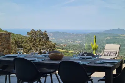 a wooden table with wine glasses and chairs on a patio at Mini villa climatisée vue mer wifi avec piscine chauffée de avriloctobre in Sollacaro