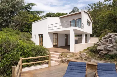 a white house on the beach with blue chairs at Villa Santa Giulia, vue mer, plage à pieds in Porto-Vecchio