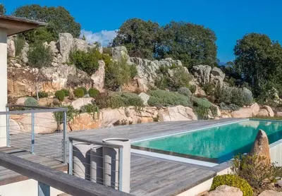 a swimming pool with a wooden deck next to a mountain at Exclusive holiday home with pool in Porto-Vecchio