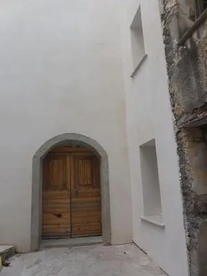 a wooden door in a white building with an archway at Saint Christophe in Omessa