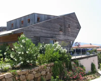 a wooden house with a stone wall and flowers at Villa avec piscine et belle vue mer proche des plages et commerces in Porticcio