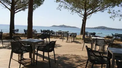 a row of tables and chairs next to the water at Kallisterra in Sainte-Lucie de Porto-Vecchio