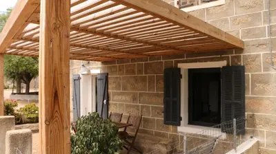 a wooden pergola on a stone wall with a patio at Casa Susini in Pianottoli-Caldarello