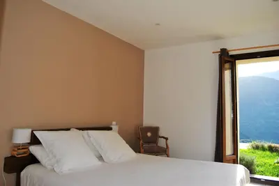 a bedroom with a bed and a window with a chair at Maison d'Hôtes Zella in Bains de Guitera