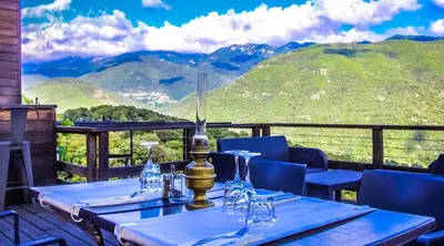 a table with wine glasses on a balcony with mountains at Maison d'Hôtes Zella in Bains de Guitera
