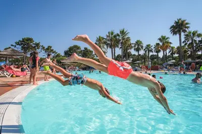 two people jumping into a swimming pool at a resort at Belambra Clubs Borgo - Pineto in Borgo