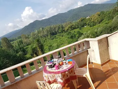 a table and chairs on a balcony with a view of mountains at House Angeli in Prunelli-di-Fiumorbo