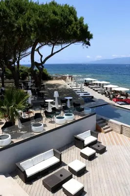 a patio with tables and chairs and the ocean at Hôtel Castel d'Orcino in Calcatoggio