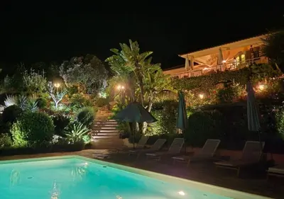 a swimming pool at night with chairs and umbrellas at Villa Mimosa in Favone