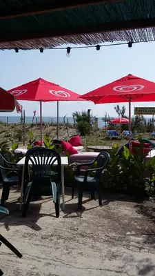 a table and chairs with red umbrellas on the beach at Camping Europa Beach in Castellare-di-Casinca