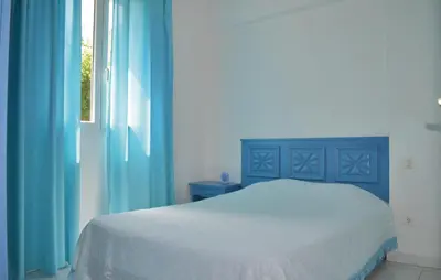 a bedroom with a bed with blue curtains and a window at Cozy Apartment In Talasani in Talasani