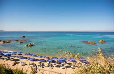a beach with chairs and umbrellas and the ocean at Hôtel Cala di Sole in Ajaccio