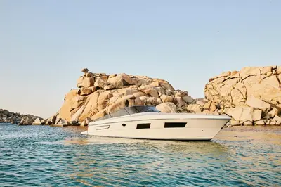 a white boat in the water next to a rocky shore at Hôtel & Spa Version Maquis Citadelle in Bonifacio
