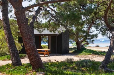 a wooden bench sitting in front of a building with trees at Camping Golfo Di Sogno in Porto-Vecchio