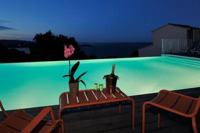 a swimming pool with two chairs and a bottle of wine at Résidence MARINA SERENA in Porto-Vecchio