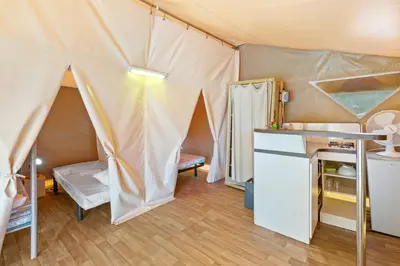 a room with a tent with a refrigerator and a table at Camping Le Damier in Pianottoli-Caldarello