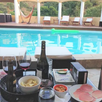 a table with glasses of wine and food next to a swimming pool at Villa SERENA in Sarrola-Carcopino