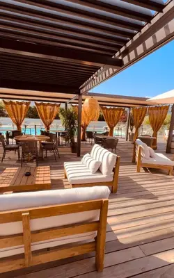 a deck with white couches and tables and chairs at Hôtel Spa Restaurant La Madrague in Lucciana