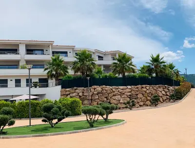 a building with palm trees and a stone wall at Résidence Les Jardins du Fort in Porticcio