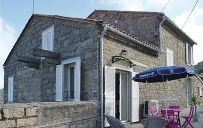 a stone house with a blue umbrella and chairs at Beautiful Apartment In Sollacaro in Sollacaro