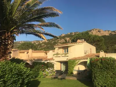 a house with a palm tree and chairs in a yard at Villa 8 au Village Marin in Porto-Vecchio