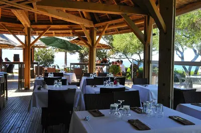 a restaurant with white tables and chairs and people at Hotel Le Ruesco in Olmeto