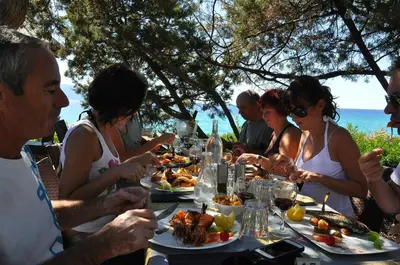 a group of people sitting at a table eating food at Hotel Le Ruesco in Olmeto
