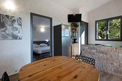 a dining room with a wooden table and a refrigerator at Résidence U LATONU - Palombaggia in Porto-Vecchio