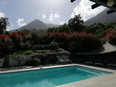 a swimming pool in a garden with mountains in the background at A Sulana Chambre d'hôtes in Valle-di-Campoloro