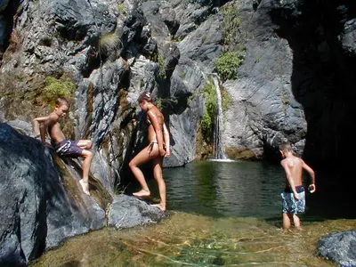 three boys in the water near a waterfall at Albaria Lodge in Saint-Florent