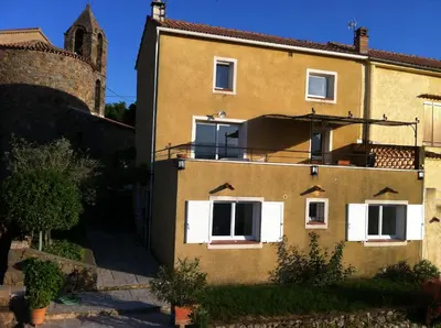 a yellow building with white windows and a tower at indé no in Sari Solenzara