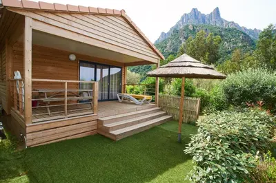 a wooden cabin with a deck with an umbrella at Camping Les Oliviers in Porto Ota