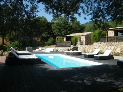 a swimming pool with lounge chairs next to a stone wall at Les Jardins de Mathieu in Porto-Vecchio
