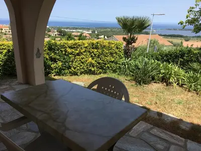 a table and chairs on a patio with a view of the ocean at Rez de Villa Vue Mer Panoramique in Furiani