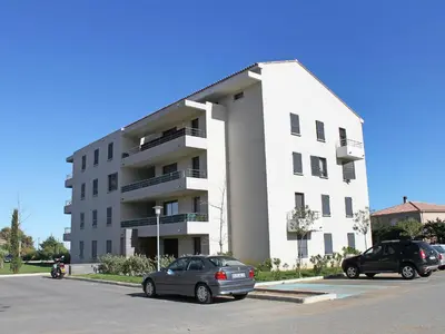 a white building with two cars parked in a parking lot at Apartment Lup - Les terrasses d'Alistro by Interhome in San-Giuliano
