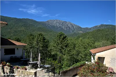 a house with a balcony with mountains in the background at Auberge des Deux Sorru in Bains de Guagno