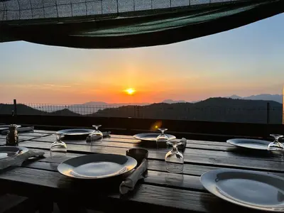 a wooden table with plates on it with the sunset in the background at Ferme auberge du col de la vaccia in Olivese