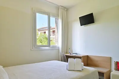 a white bedroom with a bed and a window at Hôtel de Porticcio in Porticcio