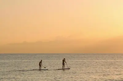 two men on paddle boards in the ocean at sunset at Hôtel de Porticcio in Porticcio