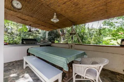 a table and chairs on a porch with a clock at Villa Trou Aux Biches in Oletta