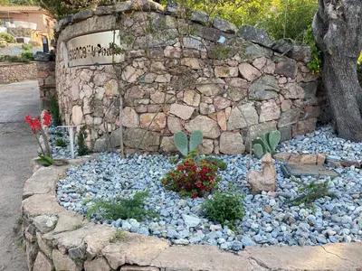 a garden with rocks and flowers in front of a stone wall at Résidence U Pirellu in Porto-Vecchio